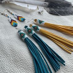 four pairs of beaded tassels are laying on a white surface next to a feather