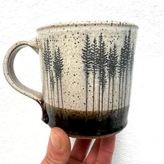 a hand holding a coffee cup with trees painted on the outside and inside, in front of a white wall