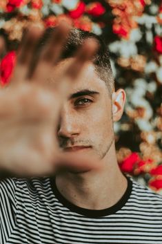 a man is making a hand gesture in front of red flowers