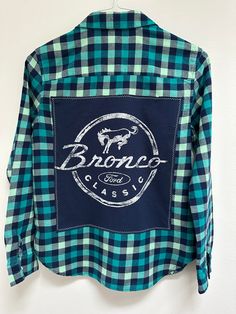 "Show off some Bronco Love in this one-of-a-kind flannel! Women's Extra Small American Eagle upcycled flannel. Navy Ford Bronco tee sewn on back. Size: Women's XS Brand: American Eagle Chest: 18\" armpit to armpit Arm Length: 22.5\" shoulder to hem Back Length: 26\" top of collar to hem Color: Navy, turquoise and mint plaid  Material: cotton  All clothing is pre-washed & comes from a smoke-free home. Wash gentle cycle, cold water  Tumble dry low Don't iron over graphic tee Please check measureme Ford Bronco Apparel, Ford Bronco Shirt, Casual Reworked Cotton Shirt, Reworked Cotton Long Sleeve Shirt, Denver Broncos Outfit, Car Shirts, Flannel Women, Upcycle Jeans, Upcycled Denim