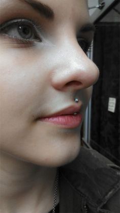 a close up of a person wearing a necklace and piercings on her nose, looking at the camera