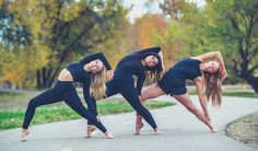 three young women are doing yoga poses on the sidewalk in front of some grass and trees