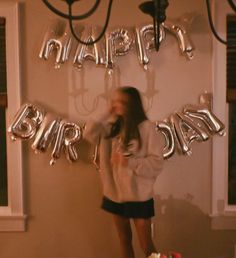 a woman standing in front of a birthday cake with balloons on the wall behind her