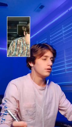 a young man with headphones on sitting in front of a blue wall and looking at the camera