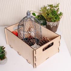 a birdcage filled with pine cones and other things sitting on a table next to potted plants