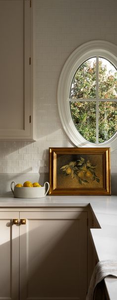 an oval window in a white kitchen with yellow fruit on the counter and sink below