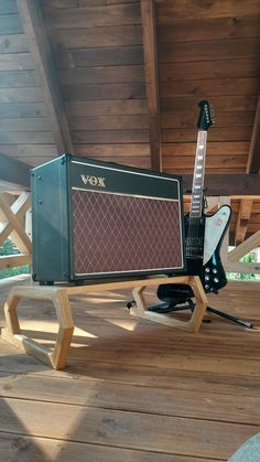 an electric guitar and amp sitting on a wooden platform under a roof in the sun