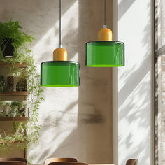 two green lamps hanging from the ceiling above a table with chairs and potted plants