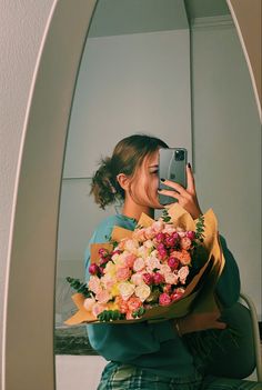 a woman taking a selfie in front of a mirror holding a bouquet of flowers