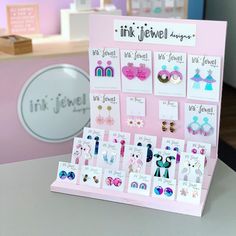 a pink display with lots of earrings on it's sides and the words ink jewel designs