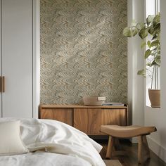 a white bed sitting next to a wooden dresser in a room with a plant on top of it