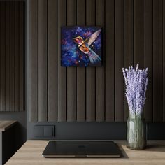 a vase filled with purple flowers sitting on top of a wooden table next to a laptop computer