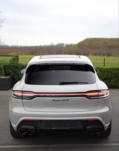 the rear end of a silver car parked in a parking lot next to a field