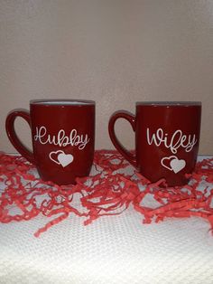 two red coffee mugs sitting on top of a white tablecloth covered table cloth