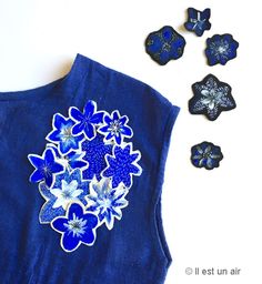 a blue vest with flowers on it next to other buttons and magnets in the shape of butterflies