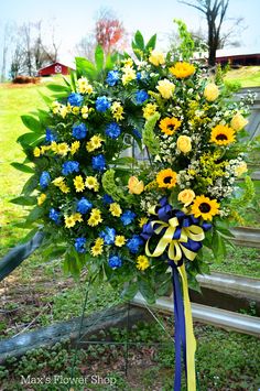 a bouquet of flowers with blue, yellow and white ribbons tied around it in front of a wooden bench