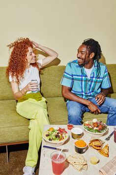 a man and woman sitting on a couch with food