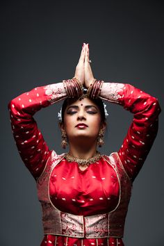 a woman in a red and gold outfit is holding her hands up to her head