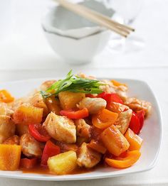 a white plate topped with chicken and veggies next to chopsticks on a table