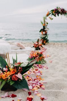 an arrangement of flowers and leaves on the sand at the beach for a wedding ceremony