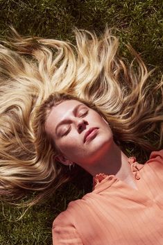 a woman laying in the grass with her eyes closed and hair blowing in the wind