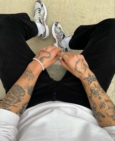 a man with tattoos on his arms and legs sitting down next to another person's feet