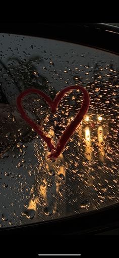 a heart is drawn on the windshield of a car in the rain with candles behind it