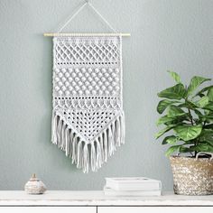 a macrame hanging on the wall next to a potted plant and books