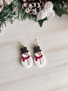 the snowman earrings are on display next to some flowers and pine cones in front of them