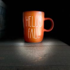 an orange coffee cup with the words hello fall written on it sitting on a wooden table