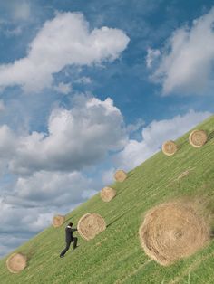 a man flying a kite over a lush green hillside covered in hay bales on a cloudy day