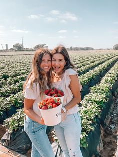 two women standing in a field with strawberries on their hands and smiling at the camera