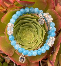 "These stunning handmade in the USA, Memory Wire Full Rosary Wrap Bracelets are made using 53 Czech Fire-Polished Aurora Borealis Crystal glass, Pearlized glass, Jasper, Mashan Jade, Quartz or Hemalyke 6 mm beads. There are sets of 8 mm Czech Fire-Polished Arora Borealis Crystal glass \"Our Father\" beads with beautiful iridescent rondelles on either side of it. A tiny Our Lady of Guadalupe-Divine Mercy or Blue Miraculous Medal and a small, round Benedictine crucifix are on either end. This full rosary is the perfect piece of Catholic jewelry for yourself, RCIA Candidates, Confirmation, Birthdays, Christmas, Graduation, Quinceañera, or Mother's Day and it's right there on your wrist when you're ready to pray the rosary. It comes in three sizes and 10 different colors. It comes in a colorfu Gift Crystal Bracelet With Czech Glass And Gemstone Beads, Czech Glass Crystal Bracelet With Gemstone Beads For Gifts, Spiritual Czech Glass Stretch Bracelet As Gift, Hand Wrapped Czech Glass Bracelet Gift, Spiritual Czech Glass Crystal Bracelet With Round Beads, Adjustable Czech Glass Spiritual Stretch Bracelet, Spiritual Czech Glass Crystal Bracelet As Gift, Spiritual Healing Glass Bracelets, Blue Spiritual Rosary Bracelet With 8mm Beads