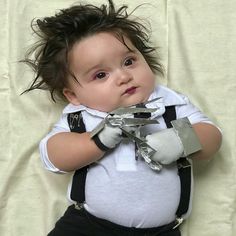 a baby boy laying on top of a bed holding a pair of scissors in his hands