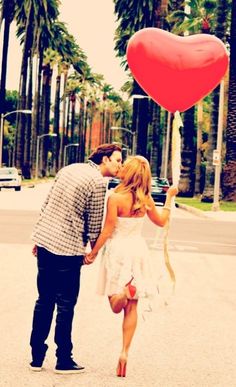 a man and woman walking down the street with a heart shaped balloon attached to them