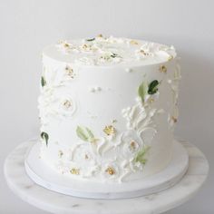 a white cake decorated with flowers and leaves on a marble platter next to a wall