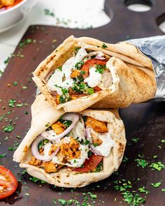 two burritos are sitting on a cutting board next to some tomatoes and herbs