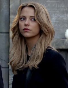 a woman with long blonde hair standing in front of a white bird on a stone wall