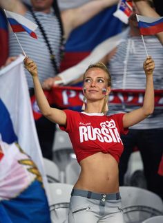 a woman holding two flags in front of other people at a soccer game, with the russian flag painted on her chest