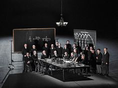 a group of men standing around a table in front of a blackboard with writing on it