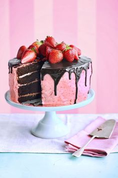 a cake with chocolate icing and strawberries sitting on a plate next to pink napkins