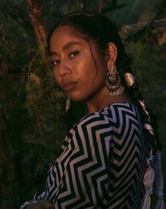 a woman in a black and white dress standing next to a tree with large earrings on her head