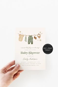 someone holding up a baby shower card with clothes hanging on a line in the background