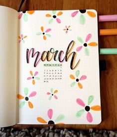 an open notebook with the word march written on it next to some colored pencils