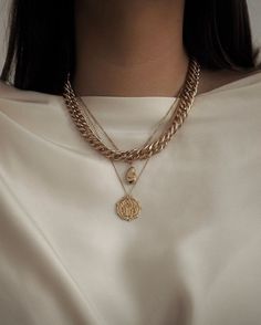 a woman wearing a gold chain necklace with a medallion on the front and an initial charm on the back