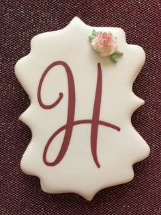 a white ceramic plaque with the letter h and a rose on it's side