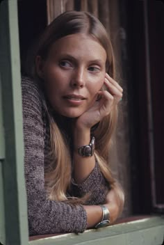 a woman with long blonde hair leaning on a window sill