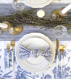 the table is set with white and blue dishes, silverware, and gold place settings