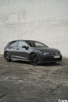 a grey car parked in front of a white brick wall with black rims on it