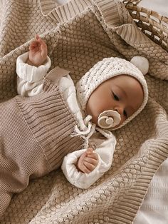 a baby in a knitted outfit laying on top of a blanket